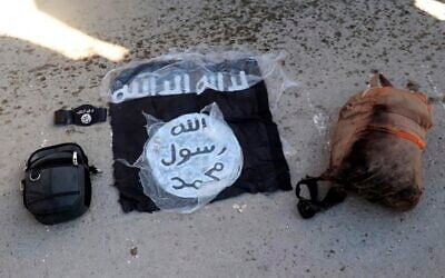 Illustration : Le drapeau du groupe terroriste sunnite État islamique (EI) et des sacs pris à des terroristes arrêtés par les Forces démocratiques syriennes, dirigées par les Kurdes, le 21 janvier 2022. (Crédit : Forces démocratiques syriennes/AP)