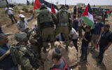 Des soldats israéliens empêchent des militants pacifistes palestiniens, israéliens et étrangers de déplacer un rocher qui bloque une route passant près de l’implantation de Mezbi yair, à Masafer Yatta, en Cisjordanie, le 13 mai 2022. (Crédit : AP/Nasser Nasser)