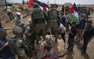 Des soldats israéliens empêchent des militants pacifistes palestiniens, israéliens et étrangers de déplacer un rocher qui bloque une route passant près de l’implantation de Mezbi yair, à Masafer Yatta, en Cisjordanie, le 13 mai 2022. (Crédit : AP/Nasser Nasser)