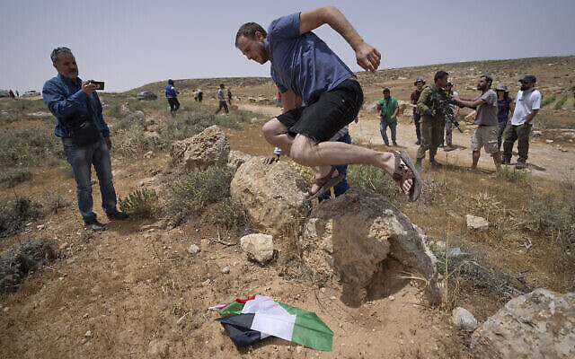 Un partisan du mouvement pro-implantation palestinien saute sur un drapeau israélien saisi à un manifestant alors que des activistes pro-paix israéliens, palestiniens et étrangers tentent d'ouvrir une route passant à proximité de l'implantation israélienne de Mezbi Yair, à Masafer Yatta, en Cisjordanie, le 13 mai 2022. (Crédit : AP Photo/Nasser Nasser) Un partisan du mouvement pro-implantation palestinien saute sur un drapeau israélien saisi à un manifestant alors que des activistes pro-paix israéliens, palestiniens et étrangers tentent d'ouvrir une route passant à proximité de l'implantation israélienne de Mezbi Yair, à Masafer Yatta, en Cisjordanie, le 13 mai 2022. (Crédit : AP Photo/Nasser Nasser)