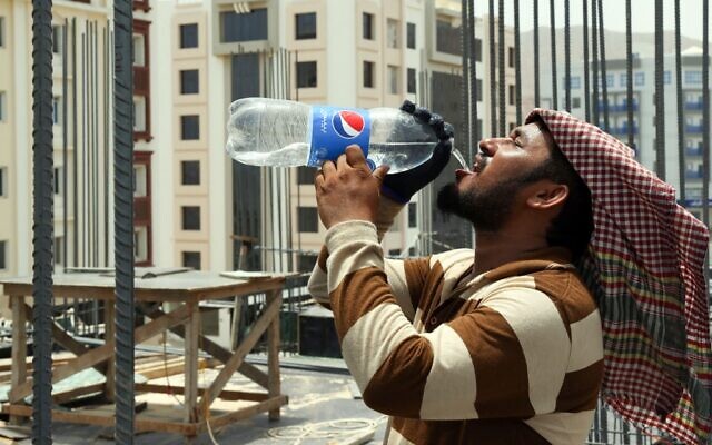 Un ouvrier étranger boit de l'eau dans une bouteille sur un chantier de construction dans la capitale omanaise, Muscat, sous une chaleur torride, le 21 juin 2022. (Crédit : MOHAMMED MAHJOUB / AFP)