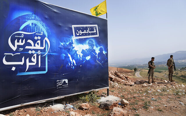 Des soldats de l'armée libanaise se tiennent à côté d'un panneau publicitaire montrant des combattants du Hezbollah avec l'inscription en arabe suivante : "Jérusalem est plus proche, nous arrivons", qui se trouve sur une colline en face de la ville israélienne de Metula, à la frontière libano-israélienne, près du village de Kfar Kila, dans le sud du Liban, dimanche 29 mai 2022. (Crédit : Hussein Malla/AP) Des soldats de l'armée libanaise se tiennent à côté d'un panneau publicitaire montrant des combattants du Hezbollah avec l'inscription en arabe suivante : "Jérusalem est plus proche, nous arrivons", qui se trouve sur une colline en face de la ville israélienne de Metula, à la frontière libano-israélienne, près du village de Kfar Kila, dans le sud du Liban, dimanche 29 mai 2022. (Crédit : Hussein Malla/AP)