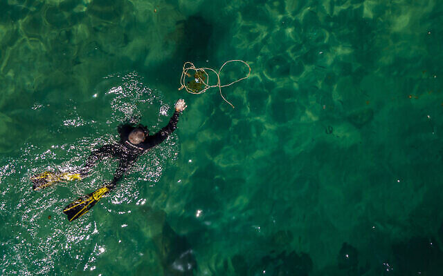 Un plongeur bénévole ramasse des déchets, à l'occasion de la Journée mondiale des océans, dans le port romain de l’ancienne Méditerranée de Césarée, en Israël, le 10 juin 2022. (Crédit : AP Photo/Ariel Schalit) Un plongeur bénévole ramasse des déchets, à l'occasion de la Journée mondiale des océans, dans le port romain de l’ancienne Méditerranée de Césarée, en Israël, le 10 juin 2022. (Crédit : AP Photo/Ariel Schalit)