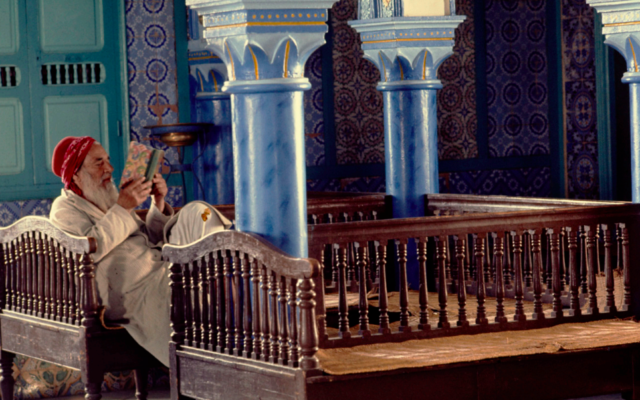 Beniamine Mazouz, vieux batlan, prie dans la synagogue de la Ghriba. Entretenus par la communauté, les batlanim passent leurs journées à la synagogue, à lire des prières et des psaumes. (Crédit : Jacques Pérez / Musée d’art et d’histoire du judaïsme, Paris)