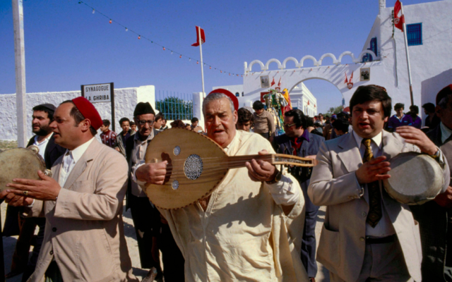 Transport de la menarah, parée d’étoffes de soie, de la Ghriba à Hara Sghira, lors du pèlerinage annuel. On reconnaît, de gauche à droite : Abraham Attia, Jacob Bchiri et Isaac Attia. Chanteur et joueur de oud, Jacob Bchiri (1912-2008) était une figure majeure de la communauté, se produisant dans les mariages, circoncisions, bar mitzvot, et bien sûr lors des pélerinages de la Ghriba et d’El Hamma. (Crédit : Jacques Pérez / Musée d’art et d’histoire du judaïsme, Paris)