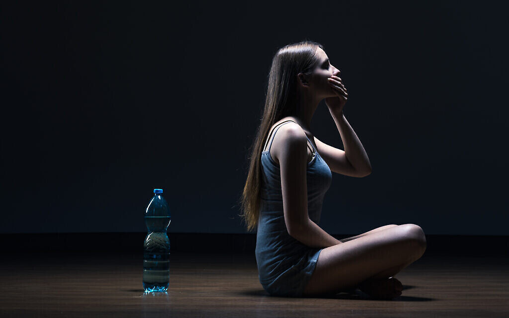 Image d'illustration. Fille anorexique assise sur le sol à côté d'une bouteille d'eau, couvrant la bouche d'une main, sur un fond sombre. (Crédit : iStock) Image d'illustration. Fille anorexique assise sur le sol à côté d'une bouteille d'eau, couvrant la bouche d'une main, sur un fond sombre. (Crédit : iStock)