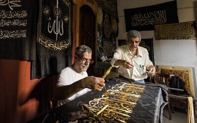 Le brodeur égyptien Ahmed Othman el-Kassabgy (à droite), dont la famille était traditionnellement responsable de la production du Kiswa, le tissu utilisé pour couvrir la Kaaba dans la Grande Mosquée de la ville sainte musulmane de La Mecque, supervise un autre employé (à gauche) qui coud avec du fil d'or un verset du Coran, le livre saint de l'islam, sur une réplique de drap qui sera vendue comme souvenir aux touristes visitant le quartier historique d'al-Hussein du Caire islamique, dans la capitale égyptienne, le 15 juin 2022. (Crédit : Khaled DESOUKI / AFP)