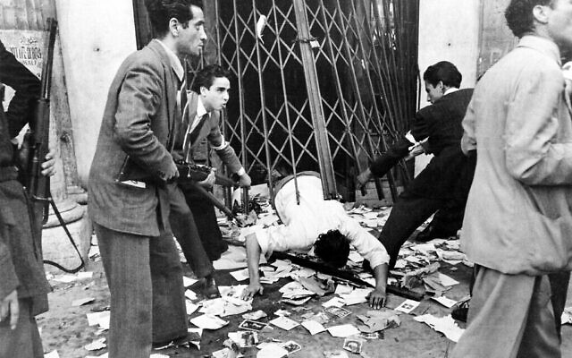 Des résistants italiens armés de fusils forcent un homme à ramper sous un rideau métallique, à la recherche de fascistes dans Rome après que la ville soit tombée aux mains des troupes alliées, le 17 juin 1944. (Crédit : AP Photo)