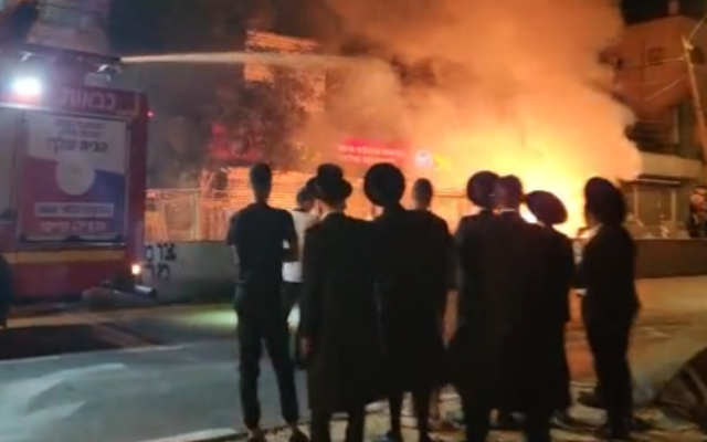 Un groupe de haredim regarde un camion de pompiers travailler à l'extinction d'un incendie causé par des émeutes à la jonction Bar Ilan à Jérusalem, le 7 juillet 2022. (Crédit: Capture d'écran/Twitter)