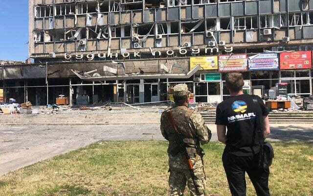 Un soldat et un civil ukrainiens regardant le centre commercial de Vinnytsia où un tir de missile russe a 25 morts, le 20 juillet 2022 (Crédit : Lazar Berman/The Times of Israel) 