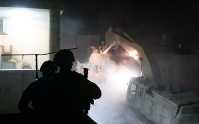 Des soldats montent la garde autour d'un bulldozer militaire, démolissant l'habitation de Youssef Sameeh Assi, accusé d'une fusillade meurtrière au mois d'avril, dans le village de Qarawat Bani Hassan, le 26 juillet 2022. (Crédit : Armée israélienne)