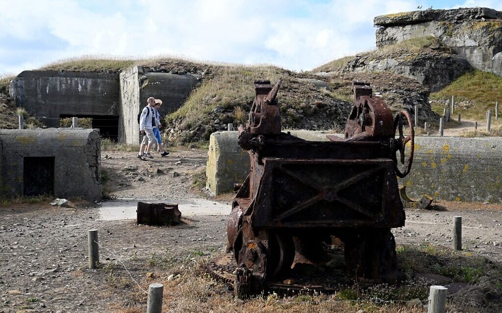 Des touristes passent devant des bunkers et des épaves de canons d'artillerie sur l'île de Cézembre, au large de Saint-Malo, le 4 août 2022. (Crédit : Damien MEYER / AFP)