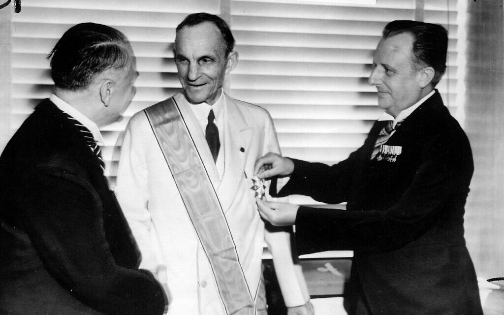 Des diplomates allemands remettent à Henry Ford, au centre, la plus haute distinction de l'Allemagne nazie pour les étrangers, la Grande Croix de l'Aigle allemand, pour ses services au Troisième Reich. Karl Kapp, consul allemand à Cleveland, épingle la médaille tandis que Fritz Heiler, à gauche, consul allemand à Detroit, lui serre la main, Detroit le 30 juillet 1938 (Crédit : AP)