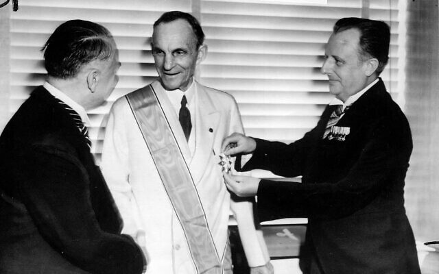 Des diplomates allemands remettent à Henry Ford, au centre, la plus haute distinction de l'Allemagne nazie pour les étrangers, la Grande Croix de l'Aigle allemand, pour ses services au Troisième Reich. Karl Kapp, consul allemand à Cleveland, épingle la médaille tandis que Fritz Heiler, à gauche, consul allemand à Detroit, lui serre la main, Detroit le 30 juillet 1938 (Crédit : AP)