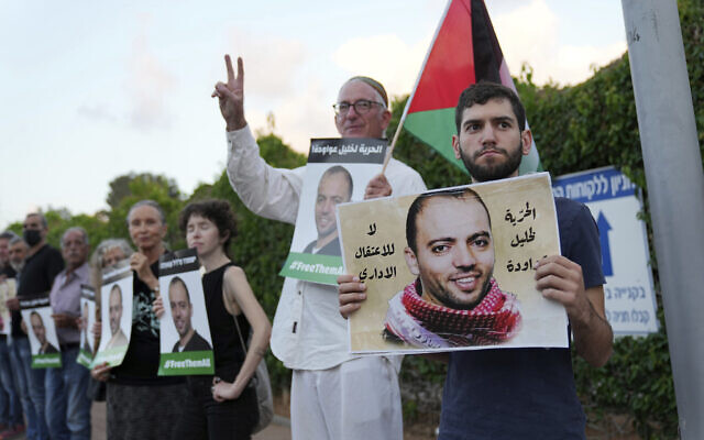 Des manifestants avec un drapeau palestinien devant l'hôpital de Be'er Yaakov où un prisonnier en grève de la faim, Khalil Awawdeh, en photo sur les pancartes, est détenu par Israël en tant que terroriste présumé, le 13 août 2022. Sur les pancartes est écrit en arabe : 'Pas de détention administrative. Liberté pour Khalil Awawdeh.' (Crédit : AP/Tsafrir Abayov) Des manifestants avec un drapeau palestinien devant l'hôpital de Be'er Yaakov où un prisonnier en grève de la faim, Khalil Awawdeh, en photo sur les pancartes, est détenu par Israël en tant que terroriste présumé, le 13 août 2022. Sur les pancartes est écrit en arabe : 'Pas de détention administrative. Liberté pour Khalil Awawdeh.' (Crédit : AP/Tsafrir Abayov)