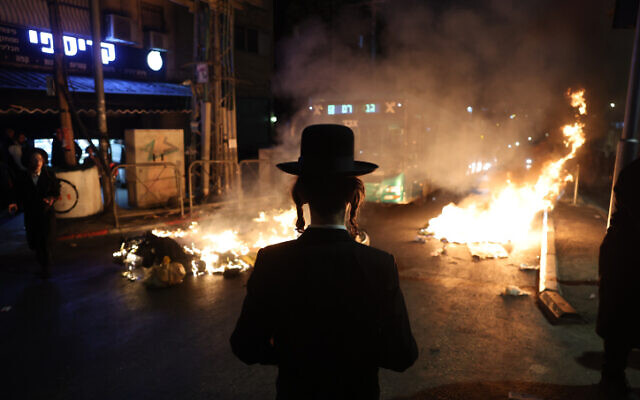 Un manifestant regardant des feux brûler lors d'une manifestation contre l'autopsie prévue d'un garçon de 4 ans, à Jérusalem, le 14 août 2022. (Crédit : Yonatan Sindel/Flash90)