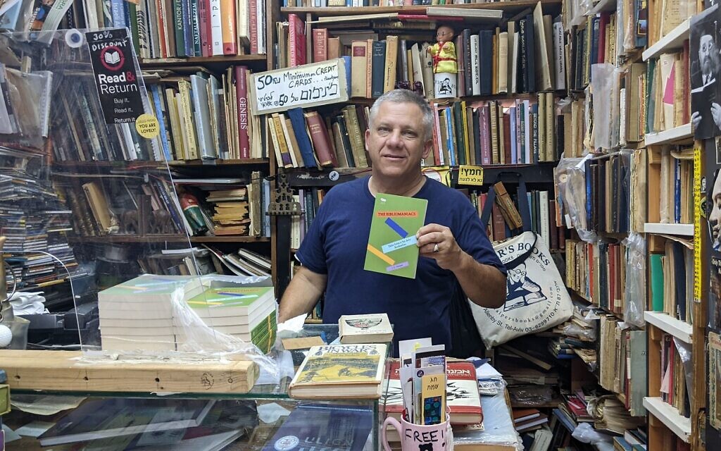 Yosef Halper, qui utilise le nom de plume J.C. Halper en clin d'œil à son nom d'origine américaine, montrant son premier livre publié dans son magasin de Tel Aviv, le 6 juillet 2022. (Crédit : Melanie Lidman/Times of Israel)