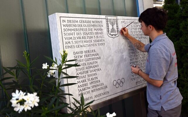 Un homme repeint l'inscription d'une plaque commémorative devant un immeuble d'habitation de la Conollystrasse 31 dans l'ancien village olympique de Munich, dans le sud de l'Allemagne, le 17 août 2022, où les membres de l'équipe olympique israélienne étaient logés pendant les Jeux olympiques de Munich de 1972. (Crédit : INA FASSBENDER / AFP) Un homme repeint l'inscription d'une plaque commémorative devant un immeuble d'habitation de la Conollystrasse 31 dans l'ancien village olympique de Munich, dans le sud de l'Allemagne, le 17 août 2022, où les membres de l'équipe olympique israélienne étaient logés pendant les Jeux olympiques de Munich de 1972. (Crédit : INA FASSBENDER / AFP)