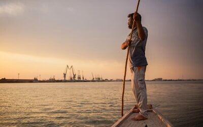 Le pêcheur irakien Naim Haddad, 40 ans, se tient pieds nus sur son bateau au coucher du soleil sur Chatt al-Arab, le confluent des fleuves du Tigre et de  l'Euphrate qui se jette dans le Golfe, près de la ville de Bassora dans le sud de l'Irak, le 12 février 2022. (Crédit : Ayman HENNA / AFP)