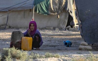 Une fillette syrienne accroupie à côté d'un bidon d'eau au camp pour personnes déplacées de Sahlah al-Banat dans la campagne de Raqa, dans le nord de la Syrie, le 19 septembre 2022. (Crédit : Delil Souleiman/AFP)
