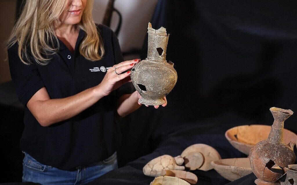 Un membre du personnel de l’Autorité israélienne des Antiquités montre l'un des récipients susceptibles d'avoir contenu de l’opium, au XIVe siècle avant notre ère, découvert sur le lieu de sépulture de Tel Yehud et exposé dans les bureaux de l’IAA à Jérusalem, le 20 septembre 2022 (Crédit : Ahmad Gharabli AFP).