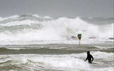 Un surfer entre dans la mer méditerranée sur une plage de Netanya, une ville côtière lors de la pire tempête de l'hiver, cette année-là, le 5 janvier 2018. (Crédit : AFP Photo/Jack Guez)