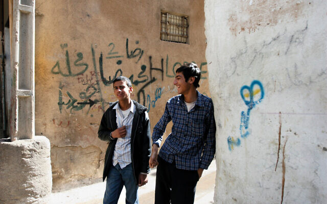 Deux jeunes hommes marchent dans un quartier juif de Shiraz. Sur le mur derrière eux, un terme péjoratif pour les Juifs est écrit en graffiti. (Crédit : Hassan Sarbakhsian/via JTA)