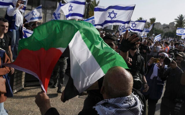 Un Palestinien brandissant son drapeau national alors que des Israéliens lèvent le leur à l'occasion de Yom Yeroushalayim, dans la Vieille Ville de Jérusalem, le 29 mai 2022. (Crédit : AP Photo/Mahmoud Illean) Un Palestinien brandissant son drapeau national alors que des Israéliens lèvent le leur à l'occasion de Yom Yeroushalayim, dans la Vieille Ville de Jérusalem, le 29 mai 2022. (Crédit : AP Photo/Mahmoud Illean)