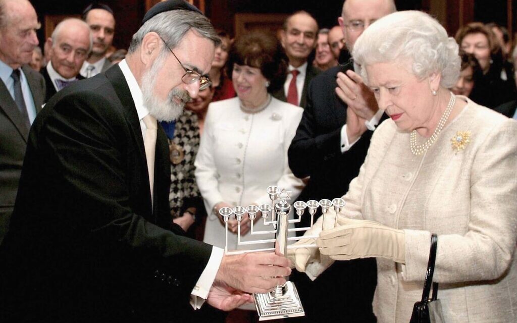Le grand rabbin britannique Jonathan Sacks, aujourd'hui décédé, offrant à la reine une ménorah lors d'une réception au palais de Saint-James pour marquer le 350e anniversaire du rétablissement de la communauté juive en Grande-Bretagne, à Londres, le 28 novembre 2006. (Crédit : Tim Graham Picture Library/Getty Images via JTA) Le grand rabbin britannique Jonathan Sacks, aujourd'hui décédé, offrant à la reine une ménorah lors d'une réception au palais de Saint-James pour marquer le 350e anniversaire du rétablissement de la communauté juive en Grande-Bretagne, à Londres, le 28 novembre 2006. (Crédit : Tim Graham Picture Library/Getty Images via JTA)