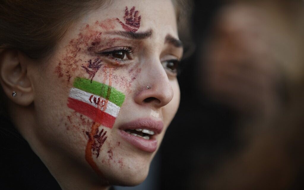 Une manifestante avec le drapeau iranien et des mains rouges dessinées sur le visage lors d'un rassemblement en soutien aux manifestations iraniennes à Paris, suite à la mort de la jeune Mahsa Amini, le 9 octobre 2022. (Crédit : Julien de Rosa/AFP) Une manifestante avec le drapeau iranien et des mains rouges dessinées sur le visage lors d'un rassemblement en soutien aux manifestations iraniennes à Paris, suite à la mort de la jeune Mahsa Amini, le 9 octobre 2022. (Crédit : Julien de Rosa/AFP)