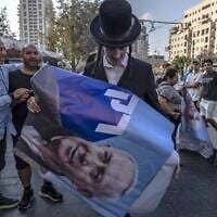 Un Juif ultra-orthodoxe avec une affiche montrant l'ex-Premier ministre israélien et leader du parti Likud Benjamin Netanyahu pendant un rassemblement de campagne, au marché Mahane Yehuda, à Jérusalem, le 20 octobre 2022. (Crédit : Menahem Kahana/AFP)