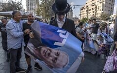 Un Juif ultra-orthodoxe avec une affiche montrant l'ex-Premier ministre israélien et leader du parti Likud Benjamin Netanyahu pendant un rassemblement de campagne, au marché Mahane Yehuda, à Jérusalem, le 20 octobre 2022. (Crédit : Menahem Kahana/AFP)