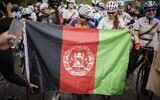 Masomah Ali Zada (C), la première cycliste afghane à participer aux Jeux olympiques en tant que membre de l'équipe de réfugiés du Comité international olympique, attend derrière un drapeau afghan sur la ligne de départ des championnats féminins de cyclisme sur route d'Afghanistan 2022 à Aigle, dans l'ouest de la Suisse, le 23 octobre 2022. (Crédit : VALENTIN FLAURAUD / AFP)