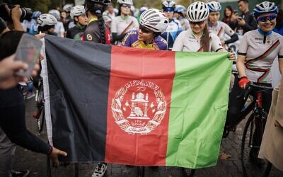 Masomah Ali Zada (C), la première cycliste afghane à participer aux Jeux olympiques en tant que membre de l'équipe de réfugiés du Comité international olympique, attend derrière un drapeau afghan sur la ligne de départ des championnats féminins de cyclisme sur route d'Afghanistan 2022 à Aigle, dans l'ouest de la Suisse, le 23 octobre 2022. (Crédit : VALENTIN FLAURAUD / AFP) Masomah Ali Zada (C), la première cycliste afghane à participer aux Jeux olympiques en tant que membre de l'équipe de réfugiés du Comité international olympique, attend derrière un drapeau afghan sur la ligne de départ des championnats féminins de cyclisme sur route d'Afghanistan 2022 à Aigle, dans l'ouest de la Suisse, le 23 octobre 2022. (Crédit : VALENTIN FLAURAUD / AFP)