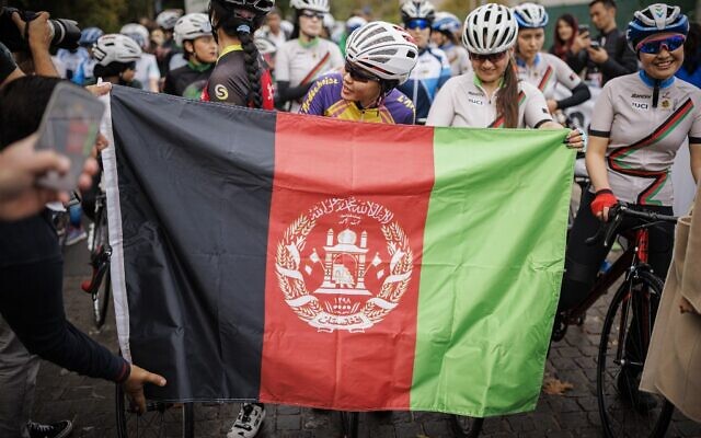 Masomah Ali Zada (C), la première cycliste afghane à participer aux Jeux olympiques en tant que membre de l'équipe de réfugiés du Comité international olympique, attend derrière un drapeau afghan sur la ligne de départ des championnats féminins de cyclisme sur route d'Afghanistan 2022 à Aigle, dans l'ouest de la Suisse, le 23 octobre 2022. (Crédit : VALENTIN FLAURAUD / AFP) Masomah Ali Zada (C), la première cycliste afghane à participer aux Jeux olympiques en tant que membre de l'équipe de réfugiés du Comité international olympique, attend derrière un drapeau afghan sur la ligne de départ des championnats féminins de cyclisme sur route d'Afghanistan 2022 à Aigle, dans l'ouest de la Suisse, le 23 octobre 2022. (Crédit : VALENTIN FLAURAUD / AFP)