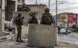 Des soldats israéliens montent la garde près de blocs de béton dans le village palestinien de Huwara, au sud de Naplouse en Cisjordanie, le 26 octobre 2022. (Crédit : MENAHEM KAHANA / AFP)