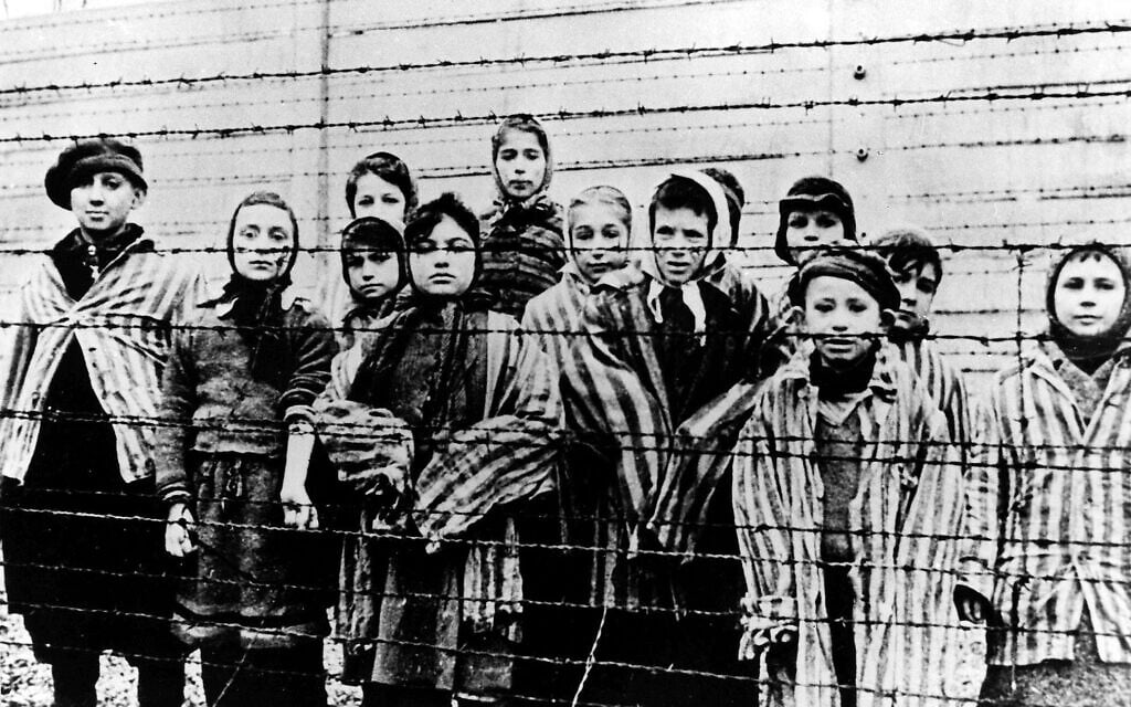 Un groupe d’enfants portant des uniformes de camp de concentration derrière des clôtures barbelées dans le camp de la mort d’Auschwitz-Birkenau, photographié juste après la libération par l’armée soviétique, en janvier 1945. (Crédit : AP Photo/Fichier)