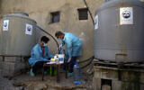 Des agents de santé de l'UNICEF mélangeant du chlore et de l'eau fraîche pour désinfecter les tentes et les sanitaires dans un camp de réfugiés syriens en réponse à une épidémie de choléra dans le village de Bhanine, dans le nord de la province du Akkar, au Liban, le 18 octobre 2022. (Crédit : Bilal Hussein/AP)