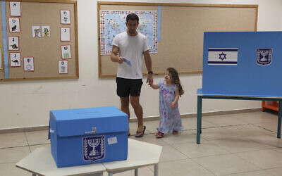 Un Israélien se dirigeant avec sa fille vers l'urne pour voter lors de la cinquième élection en Israël en moins de quatre ans dans un bureau de vote de Tel Aviv, le 1er novembre 2022. (Crédit : Jack Guez/Pool Photo via AP)