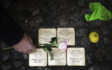 Juergen Schulz, un habitant du quartier, déposant une fleur après avoir poli les "Stolpersteine" ou "pierres d'achoppement" commémorant les personnes déportées et tuées par les nazis, devant sa maison à Berlin, en Allemagne, le 9 novembre 2021. (Crédit : Markus Schreiber/AP)