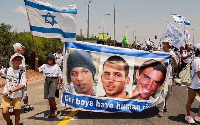 Des manifestants d'Ashkelon défilent avec une banderole en l'honneur du civil israélien captif Avera Mengistu et des soldats décédés Oron Shaul et Hadar Goldin, et arrivent au kibboutz Karmia, le 5 août 2022. (Crédit : Jack Guez/AFP)