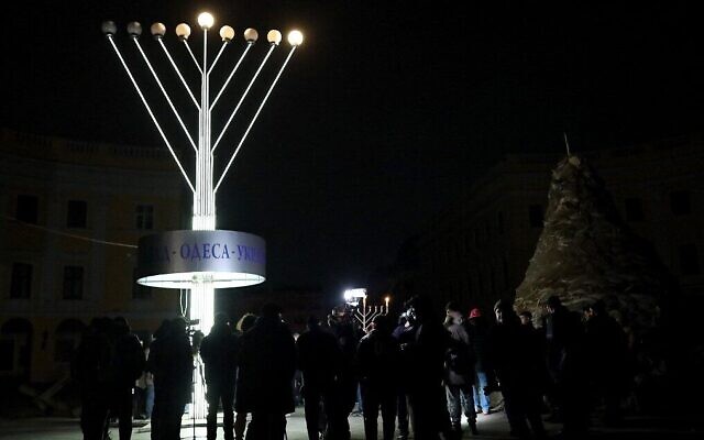 Des membres de la communauté juive se tiennent près d'une hanoukkiah géante lors d'ne cérémonie pour la fête juive de Hanoukka dans la ville ukrainienne d'Odessa, pendant une panne d'électricité, le 18 décembre 2022, lors de l'invasion russe de l'Ukraine. (Crédit : Oleksandr GIMANOV / AFP) Des membres de la communauté juive se tiennent près d'une hanoukkiah géante lors d'ne cérémonie pour la fête juive de Hanoukka dans la ville ukrainienne d'Odessa, pendant une panne d'électricité, le 18 décembre 2022, lors de l'invasion russe de l'Ukraine. (Crédit : Oleksandr GIMANOV / AFP)