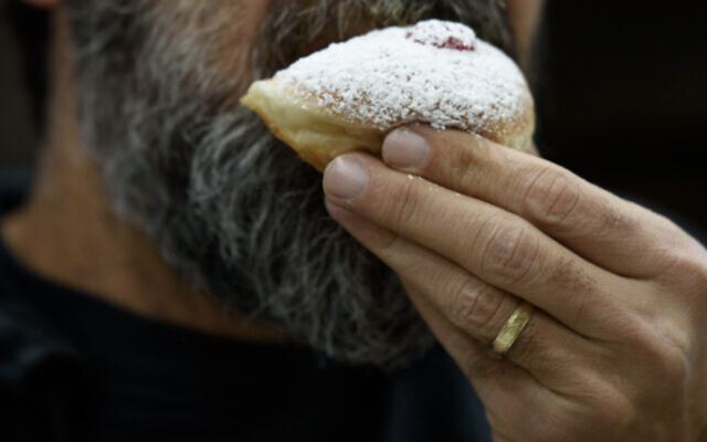 Illustration : Un homme mangeant une soufganiyah, un beignet traditionnel de Hanoukka, quelques jours avant la fête des Lumières, à Kiryat Shmona, dans le nord d'Israël, le 14 décembre 2022. (Crédit : Ayal Margolin/Flash90)