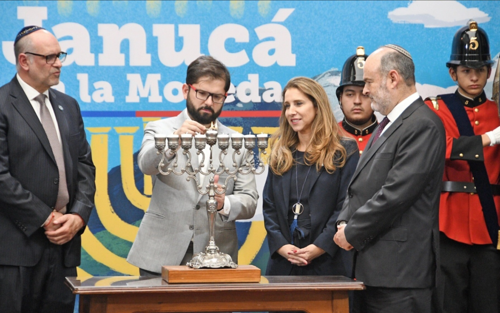  Le président chilien Gabriel Boric allumant une menorah symbolique avant la fête de Hanoukka, accompagné du président et du vice-président de la communauté juive du Chili, Gerardo Gorodischer et Ariela Agosin, et de l'aumônier de La Moneda, le rabbin Eduardo Waingortin, au palais de La Moneda, au Chili, le 16 décembre 2022. (Crédit :  La communauté juive chilienne/JTA)