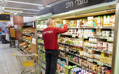 Un employé remplissant un rayon de produits laitiers au supermarché Shufersal Deal, à Katsrin, sur le plateau du Golan, le 1ᵉʳ juillet 2022. (Crédit : Michael Giladi/Flash90)