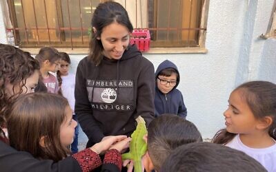 Des enfants de l’école primaire Bine B, près de Deir el-Asad dans le nord d’Israël, se rassemblent autour d’un iguane, le 28 novembre 2022. (Crédit : Sue Surkes/Times of Israel)