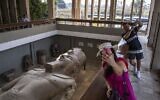 Des touristes regardent la statue colossale (10 mètres de long) en calcaire du pharaon égyptien Ramsès II (1279-1213 av. J.-C.), trouvée à l'origine dans les ruines du temple de Ptah voisin et maintenant exposée dans son enceinte spéciale dans les ruines de l'ancienne Memphis (Mennefer) à Mit Rahina, au sud de la capitale égyptienne, Le Caire, le 30 octobre 2022. (Crédit : Amir MAKAR / AFP)