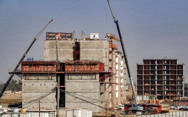 Des ouvriers de la construction se tiennent sous une grue au sommet d'un immeuble d'habitation inachevé dans la capitale irakienne, Bagdad, le 16 décembre 2022. (Crédit : AHMAD AL-RUBAYE / AFP) Des ouvriers de la construction se tiennent sous une grue au sommet d'un immeuble d'habitation inachevé dans la capitale irakienne, Bagdad, le 16 décembre 2022. (Crédit : AHMAD AL-RUBAYE / AFP)