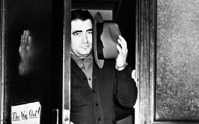 Charles Workman, dit "The Bug" , tente de se protéger le visage avec son chapeau alors qu'il quitte le bureau du procureur de Brooklyn, New York, le 30 mars 1941, pour être enregistré comme fugitif dans un poste de police voisin. Workman a été inculpé à Newark, New Jersey, pour le meurtre de Dutch Schultz en 1935. (Crédit : AP)