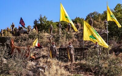 Les combattants du Hezbollah posent avec les drapeaux jaunes du groupe terroriste et des drapeaux portant les noms de personnalités chiites vénérées (en noir) pendant une cérémonie de pose de la première pierre d'un site de "tourisme jihadiste", dans un camp qui était dirigé par le Corps des gardiens de la révolution iranien pour former les combattants du Hezbollah, dans la région de Janta, à l'Est du pays, le 19 août 2022. (Crédit : AFP)